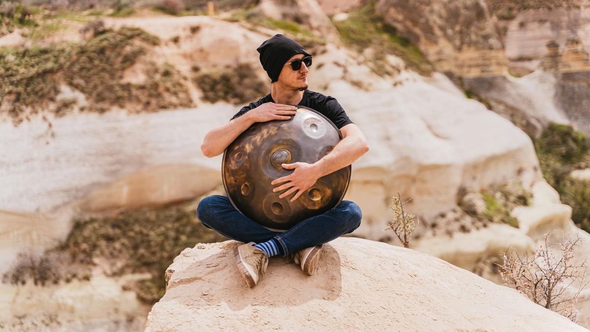 Person sitting among sandy rocks, holding a handpan against their chest